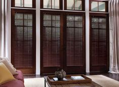 a living room filled with furniture and large windows covered in wooden shutters, along with a cat sitting on the coffee table