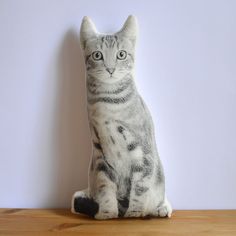 a grey and white cat sitting on top of a wooden table next to a wall