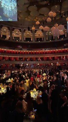 a large group of people sitting at tables in front of a screen with lights on it