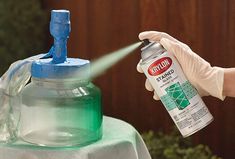 a person in white gloves spraying water onto a table with a green and blue spray bottle