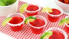 several glasses filled with red liquid and limes next to strawberries on a table