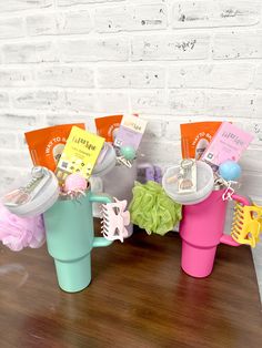 three colorful cups with hair clips on them sitting on a table next to a brick wall