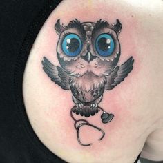 an owl with blue eyes and a stethoscope tattoo on the back of a woman's shoulder