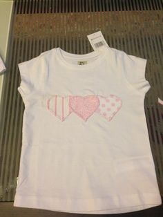 a white t - shirt with pink hearts and polka dots on the chest is sitting on a table