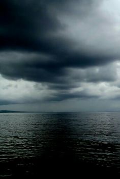 the sky is filled with dark clouds over the water and there are no people in it