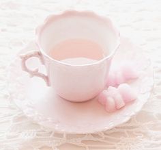 a white cup and saucer with pink pom - poms on a lace tablecloth