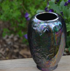 a black vase sitting on top of a wooden table in front of purple and green flowers