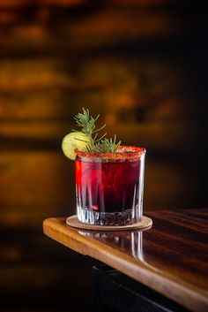 a red drink sitting on top of a wooden table next to a slice of cucumber