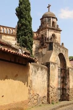 an old building with a cross on the top and a tree growing out of it