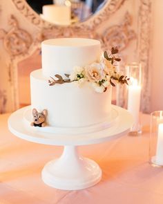 a white wedding cake with flowers on top and candles in the background at a reception