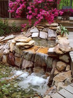 a small waterfall in the middle of a garden with rocks and flowers on either side