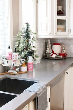 a christmas tree in the corner of a kitchen with white cabinets and silver counter tops