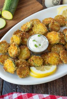 a white plate topped with fried zucchini next to a cup of ranch dressing