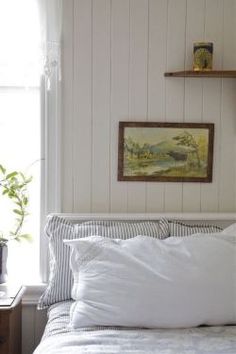 a bed with white linens and pillows in a bedroom next to a painting on the wall