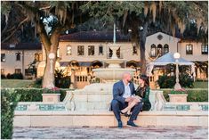 a man and woman sitting on a bench in front of a mansion