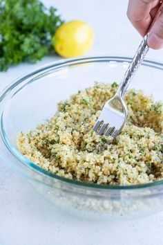 someone using a fork to mix up food in a glass bowl with lemons and parsley