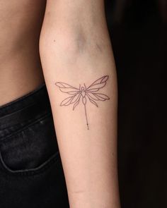 a woman's arm with a small dragonfly tattoo on the back of her left arm