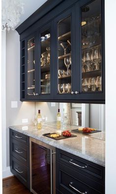 a kitchen with black cabinets and white marble counter tops, wine glasses on the glass doors