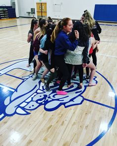 a group of girls huddle together in the middle of a gym floor with blue and white designs on it