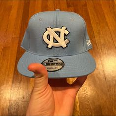 the north carolina university hat is on display in someone's hand, with wood flooring behind it