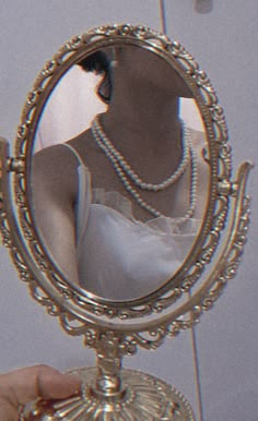 a woman looking at herself in the mirror with pearls on her neck and necklaces