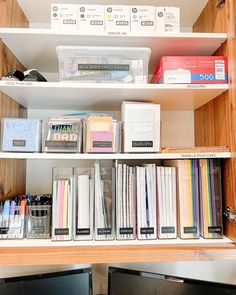 two computer monitors sitting next to each other on a wooden shelf filled with books and binders