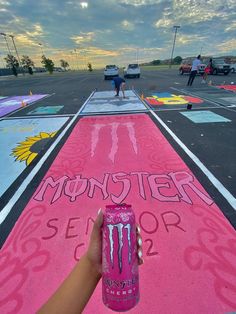 someone holding up a can of monster energy drink in the middle of a parking lot