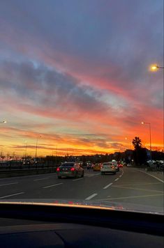 cars driving down the road at sunset with colorful clouds in the sky and street lights