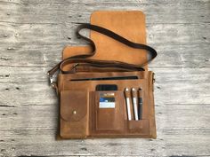 a brown leather bag sitting on top of a wooden table next to a cell phone