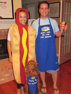 a man and woman in costumes standing next to a dog wearing a hot dog costume