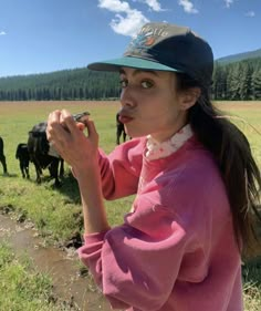 a woman in a pink shirt and hat standing next to some black cows on a field