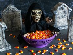 a bowl filled with candy sits in front of two tombstones and one is wearing a skeleton costume