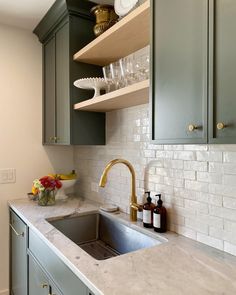 a kitchen with green cabinets and white marble counter tops, gold faucet handles