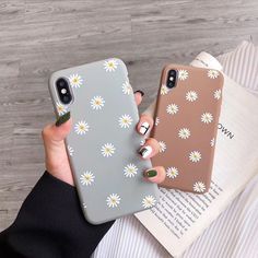 a woman is holding up her phone case with daisies on the front and back