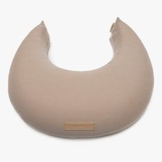 the neck pillow is beige and has a gold tag on it's side, along with a white background