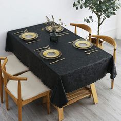 a black table cloth with gold plates on it and a potted tree in the background