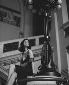 black and white photograph of a woman sitting on top of a stair case next to a lamp