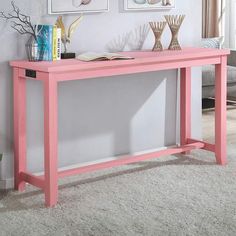 a pink console table in front of a white wall with pictures on the wall behind it