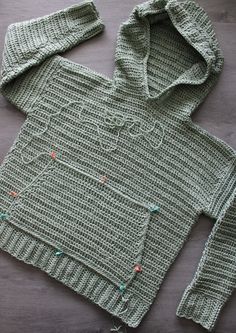 a green knitted sweater sitting on top of a wooden table