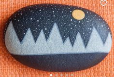 a painted rock with mountains on it and a yellow dot in the middle is sitting on an orange cloth