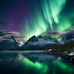 the northern lights shine brightly over snow covered mountains and water in this landscape photo taken at night