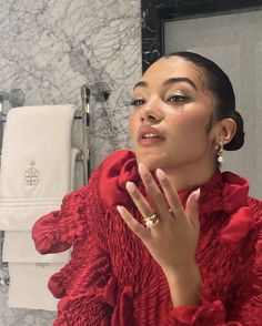 a woman with her hand on her face in front of a bathroom mirror wearing a red dress