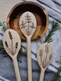 three wooden spoons with designs on them sitting next to a bowl filled with leaves