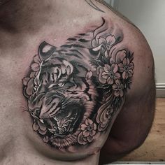 a man's chest with a tiger and flowers tattoo design on it, while he is wearing no shirt