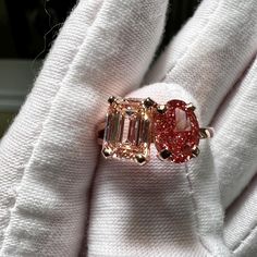 a close up of a person wearing a ring with an emerald and pink diamond on it