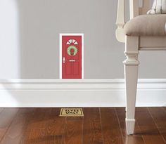 a red door with a wreath on it is in front of a white chair and wooden floor