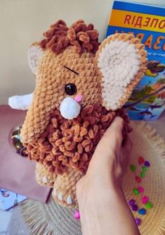 a hand holding a small stuffed animal on top of a table next to a book