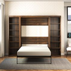 a bed sitting in front of a wooden bookcase next to a white chair and window