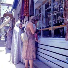 a woman standing in front of a store talking on her cell phone while wearing a dress