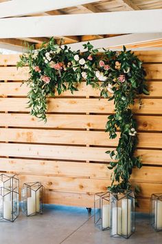 a wooden wall with candles and greenery on the top, along with lanterns in front of it